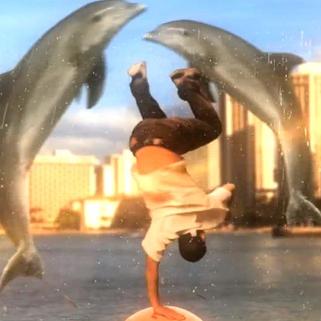 A man breakdancing, doing a handstand, with dolphins jumping in the background.